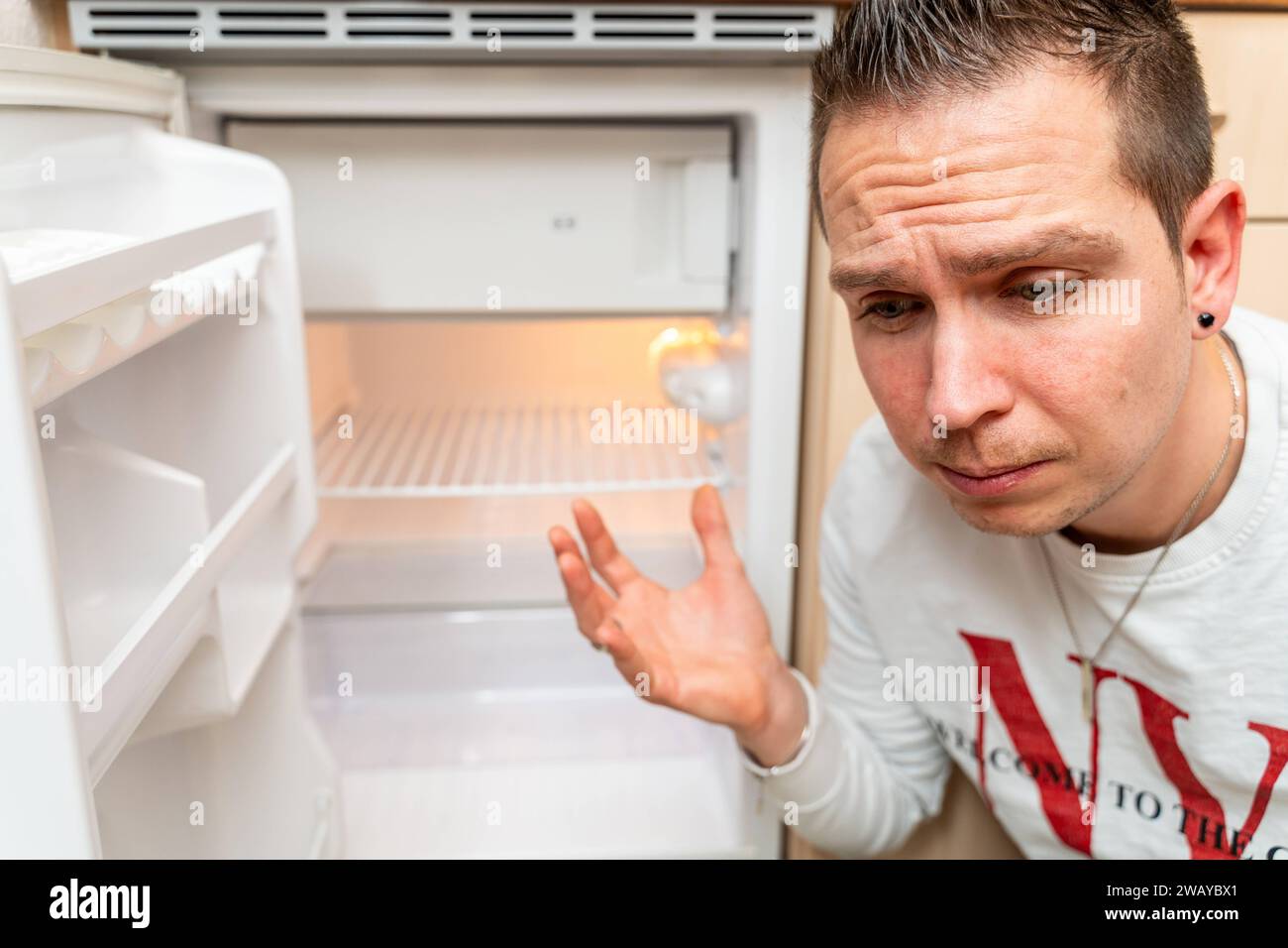 Bayern, Deutschland - 6. Januar 2024: Ein trauriger Mann vor einem leeren Kühlschrank, Inflations- und Armutskonzept *** ein Trauriger Mann vor einem leeren Kühlschrank, Inflations- und Armutskonzept Stockfoto