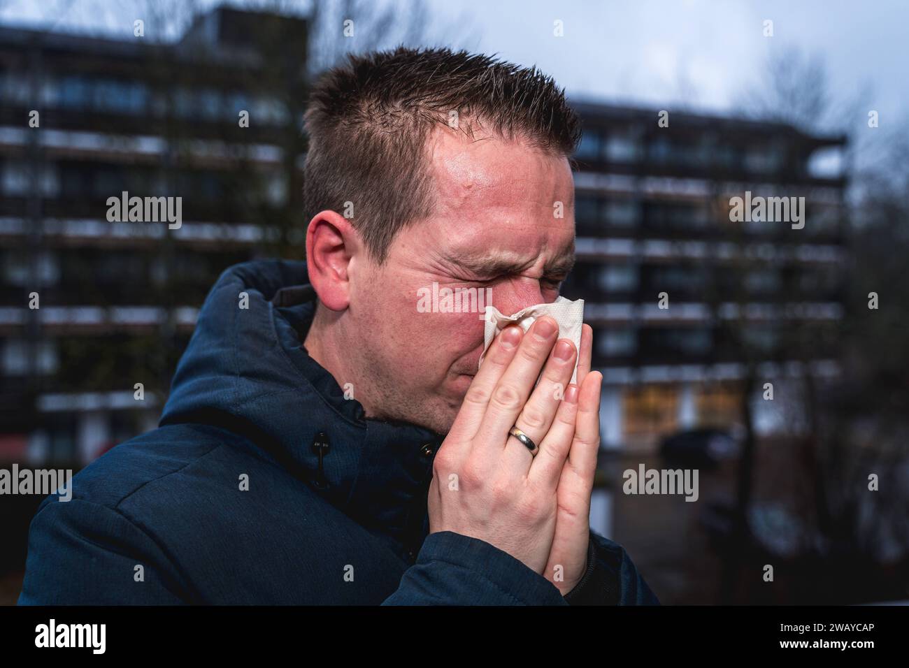 Bayern, Deutschland - 6. Januar 2024: Ein kranker Mann mit Erkältung bläst sich mit einem Papiertaschentuch die Nase *** ein kranker erkälteter Mann putzt sich mit einem Papiertaschentuch die Nase Stockfoto