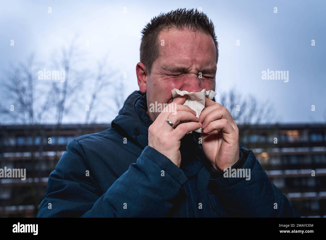 Bayern, Deutschland - 6. Januar 2024: Ein kranker Mann mit Erkältung bläst sich mit einem Papiertaschentuch die Nase *** ein kranker erkälteter Mann putzt sich mit einem Papiertaschentuch die Nase Stockfoto