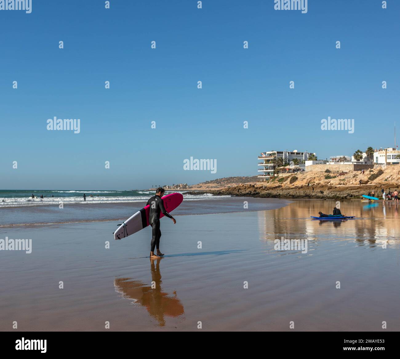 Ein Surfer, der am Strand entlang läuft und ein Surfbrett hält Stockfoto