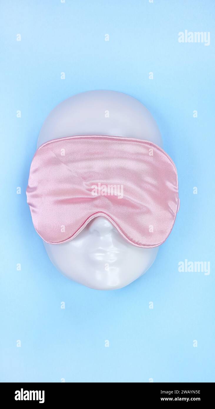 Pinkfarbene Schlafaugenmaske auf weißem Schaufensterpuppen-Gesicht auf blauem Hintergrund, Schlafstörung. Valentinstag. Feiertage, Kopfzubehör. Kunststofffläche. Stockfoto