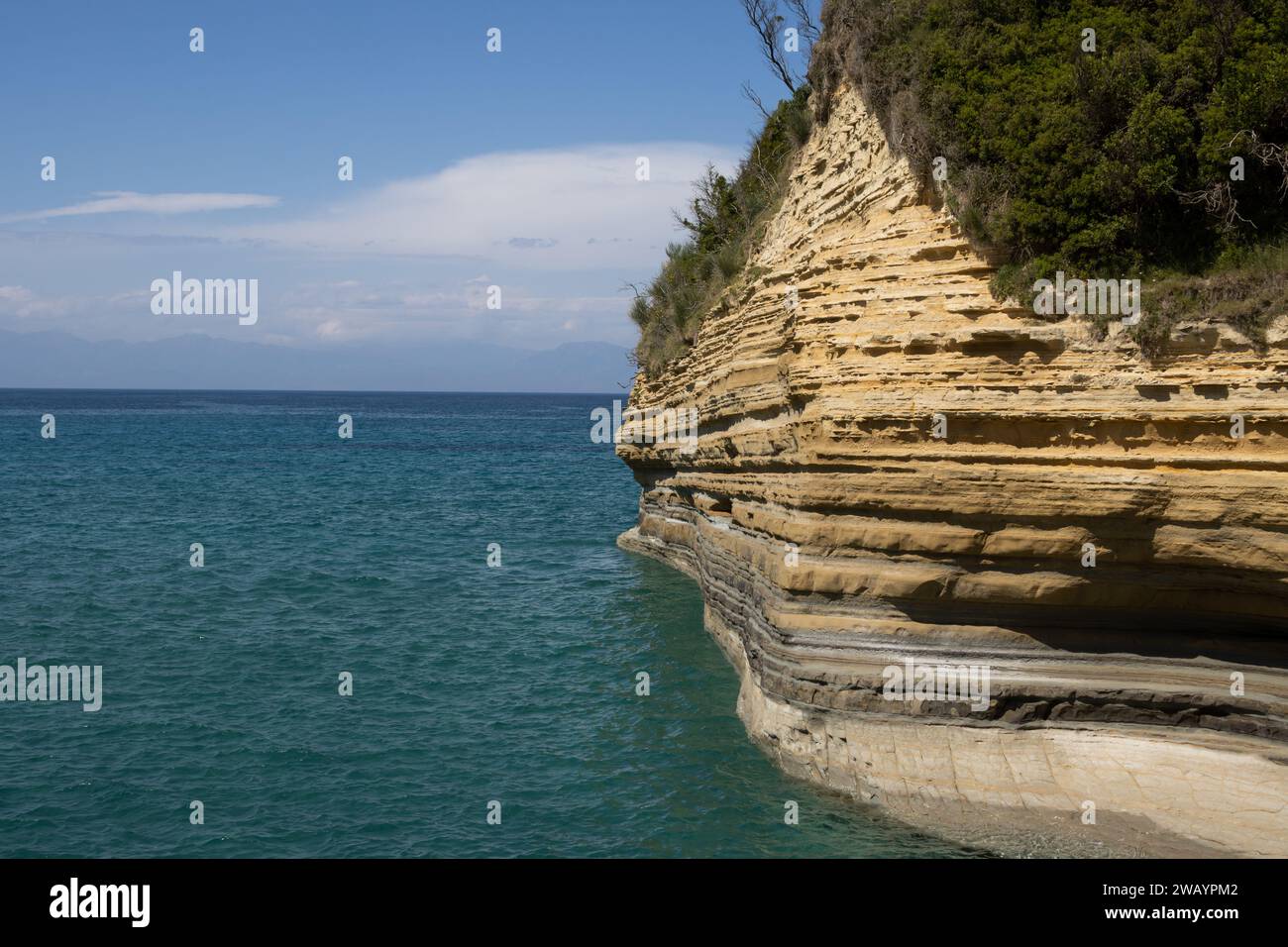 Natürliche Felsformationen an der Küste des Ionischen Meeres (Mittelmeer) im nördlichen Teil der Insel. Ruhiges Wasser des Meeres. Blauer Himmel mit hellen Wolken Stockfoto