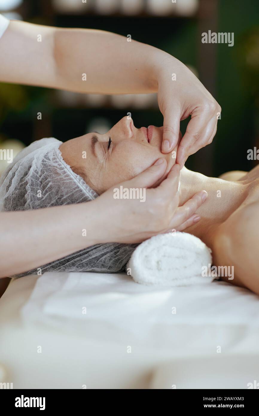 Gesundheitszeit. Medizinischer Massagetherapeut im Massageschrank, der das Gesicht des Kunden auf dem Massagetisch massiert. Stockfoto