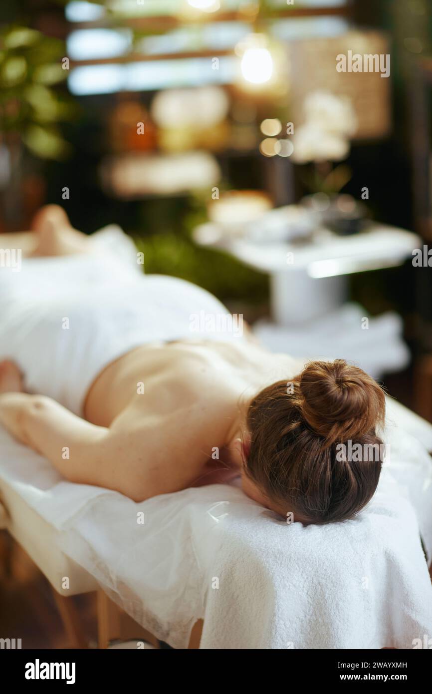 Gesundheitszeit. Entspannte, moderne Frau mittleren Alters im Spa-Salon, die auf einem Massagetisch liegt. Stockfoto