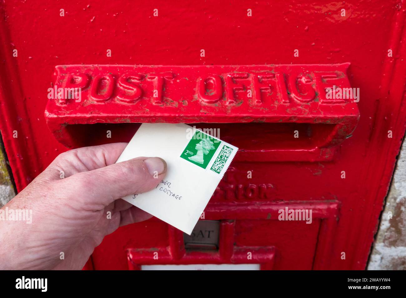 Einen Brief der zweiten Klasse in einem roten Briefkasten der Royal Mail verschicken. Stockfoto