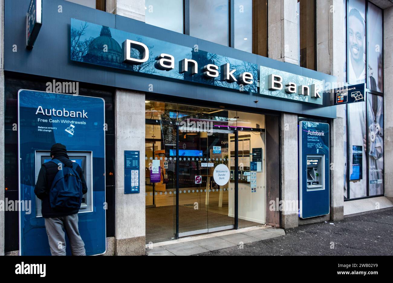 Ein Mann, der neben einem Geldautomaten der Danske Bank in Belfast, Nordirland, steht. Stockfoto