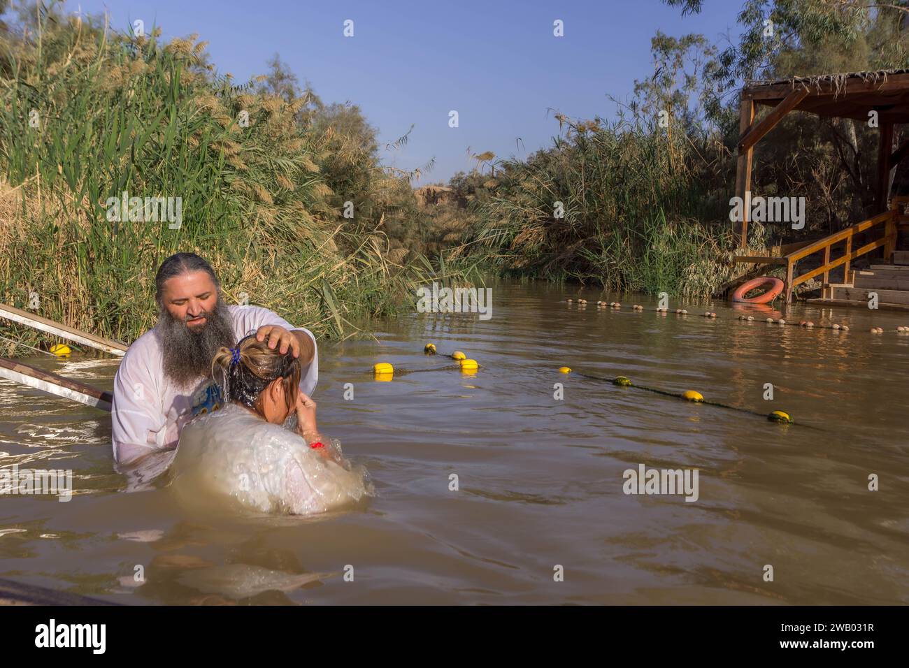 Der christliche Priester tauft Frau im Wasser des Jordaniens an der Grenze zwischen Palästina und Jordanien in Qasr al-Yahud, der Taufstätte Jesu Christi Stockfoto