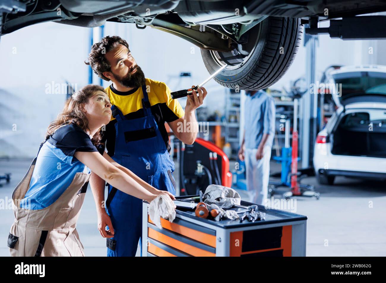 Mechaniker arbeiten an der Wartung defekter Fahrzeuge zusammen und prüfen auf defekte Reifen. Geschickte Reparaturwerkstätten arbeiten gemeinsam an der Reparatur des Fahrzeugs und diskutieren die besten Optionen Stockfoto