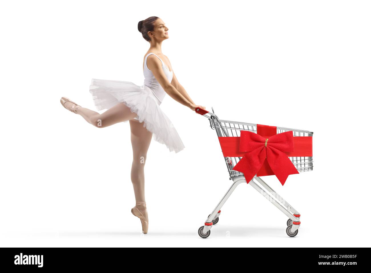 Profilaufnahme einer Ballerina in einem weißen Tutu-Kleid tanzend und schiebend einen Einkaufswagen gebunden mit roter Schleife isoliert auf weißem Hintergrund Stockfoto