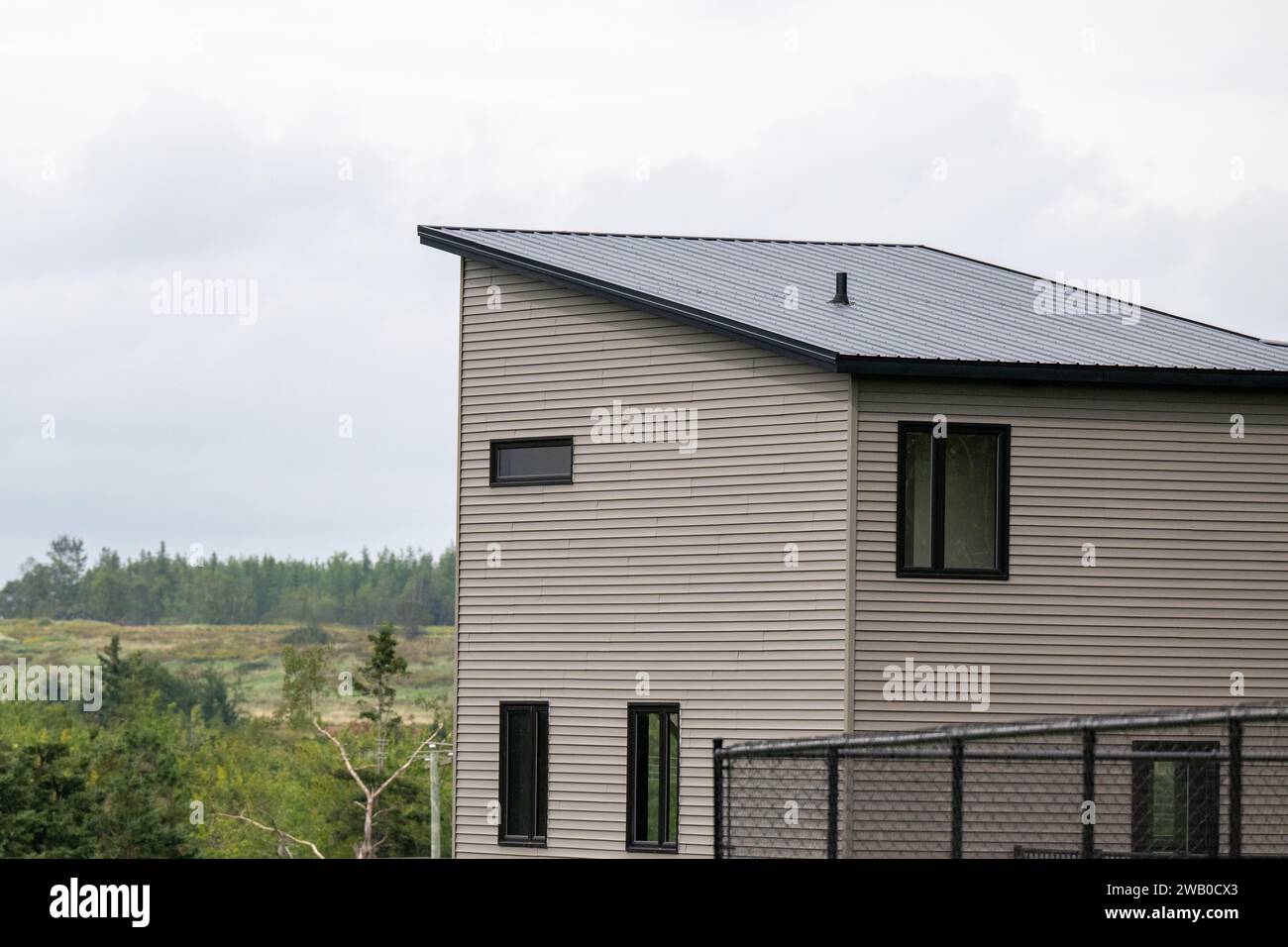 Die Außenecke eines modernen hölzernen, winzigen Hauses. Es hat graue Vinylwände mit schwarzer Verkleidung, geschlossene Glasfenster, ein schräges Flachdach und eine schwarze Metallrückseite Stockfoto