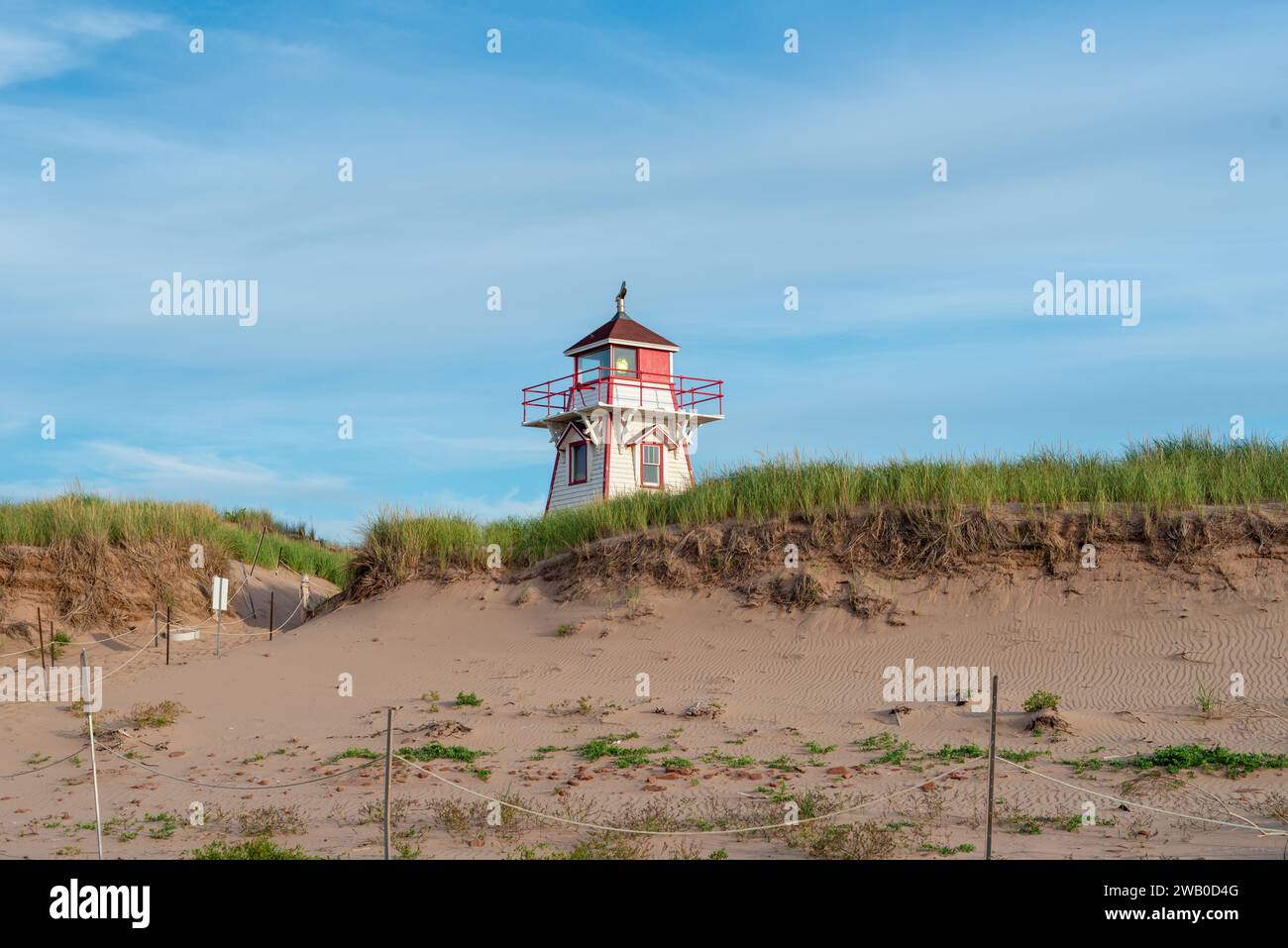 Ein weiß-roter, vierseitiger Holzleuchtturm. Es gibt Fenster mit roter Verkleidung. Eine Galerie umgibt die Struktur. Die Laterne ist an Stockfoto