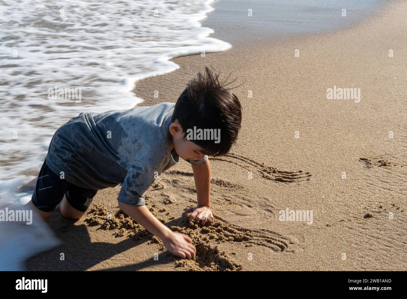 Kleiner asiatischer Junge, der im Sand am Strand spielt Stockfoto