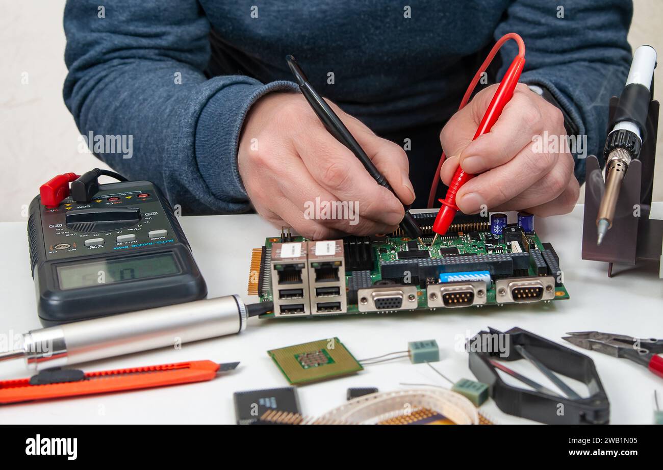 Nahaufnahme der Hände eines Technikers in einer Werkstatt. Der Servicebetrieb verwendet ein Multimeter, um die Parameter eines elektronischen Geräts auf einem Tisch zu messen. Stockfoto