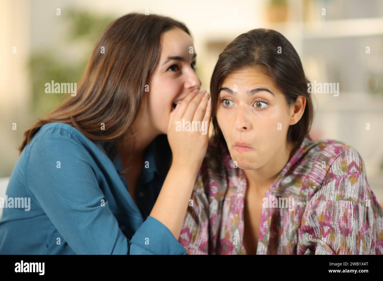 Eine Klatschfrau erzählt einem verwirrten Freund zu Hause ein Geheimnis Stockfoto