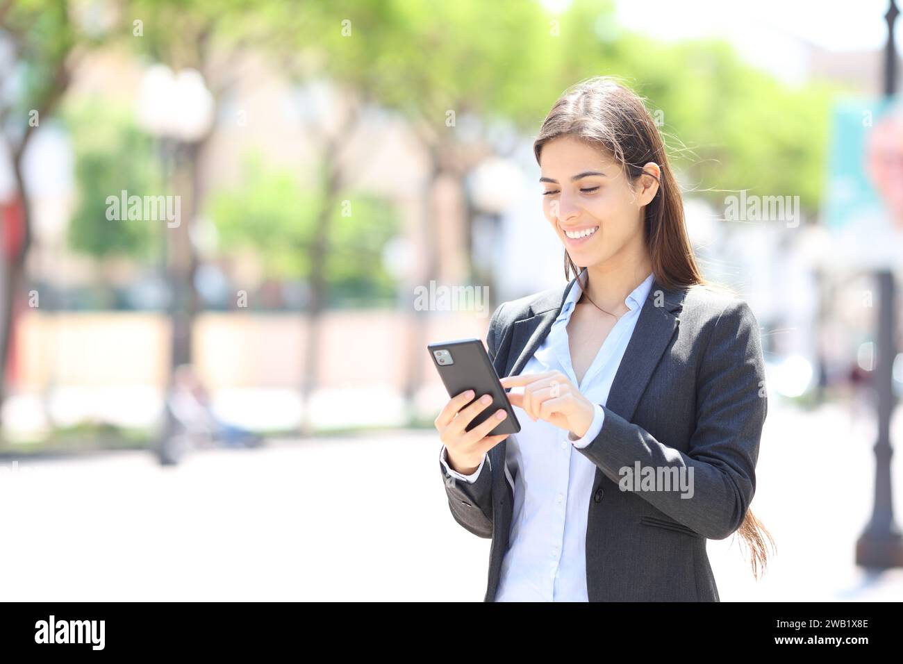 Glücklicher Manager überprüft das Handy, wenn er auf der Straße läuft Stockfoto