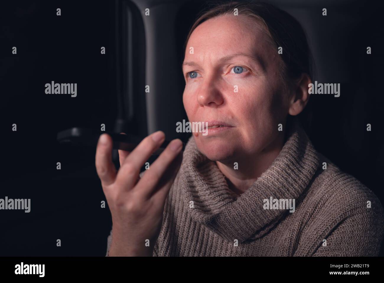 Frau, die auf dem Handy von der Rückbank des Autos auf einem Roadtrip in der Nacht spricht, selektiver Fokus Stockfoto