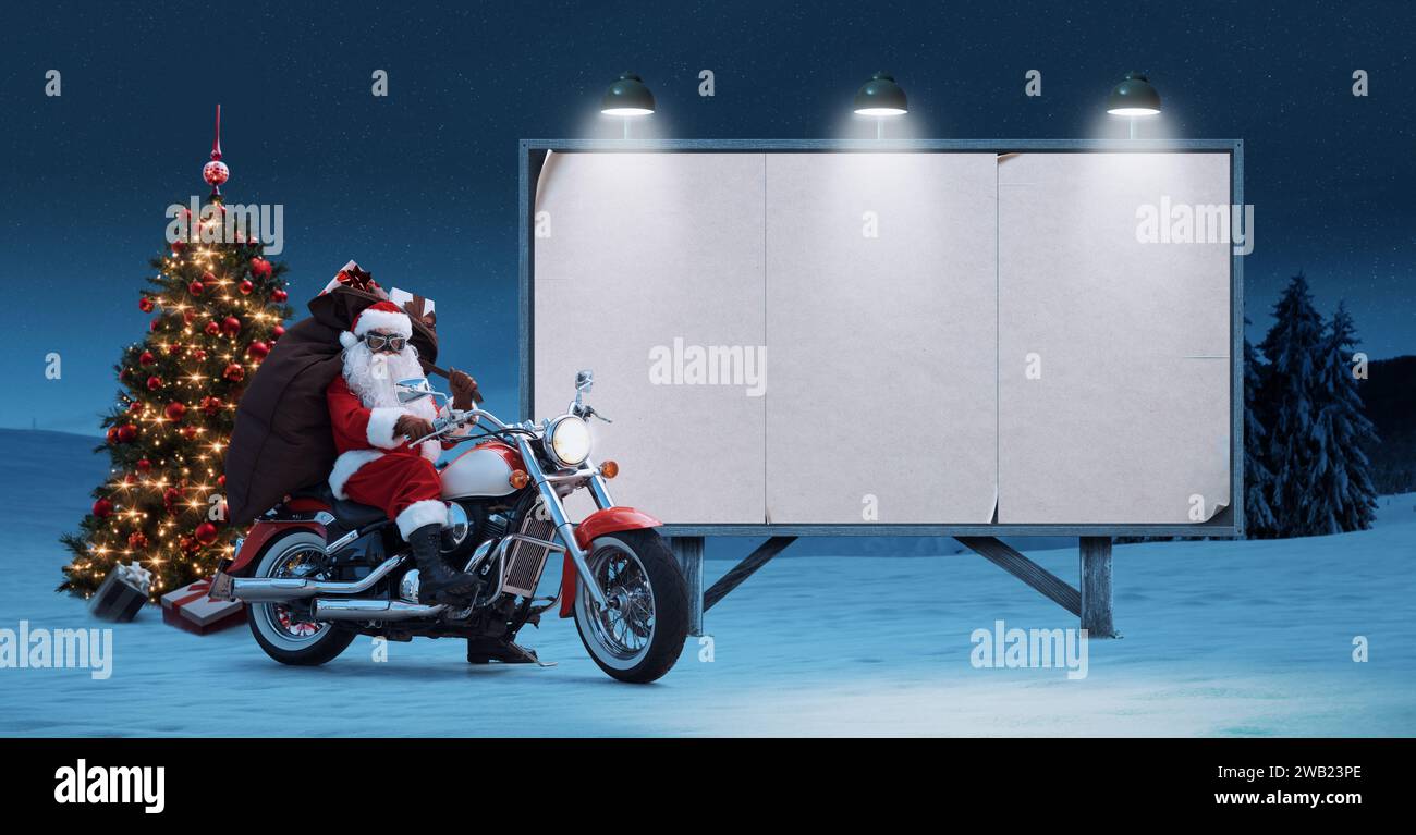 Unkonventioneller Weihnachtsmann mit Motorrad und unbelegtem Werbetafel, Konzept für Weihnachtswerbung Stockfoto