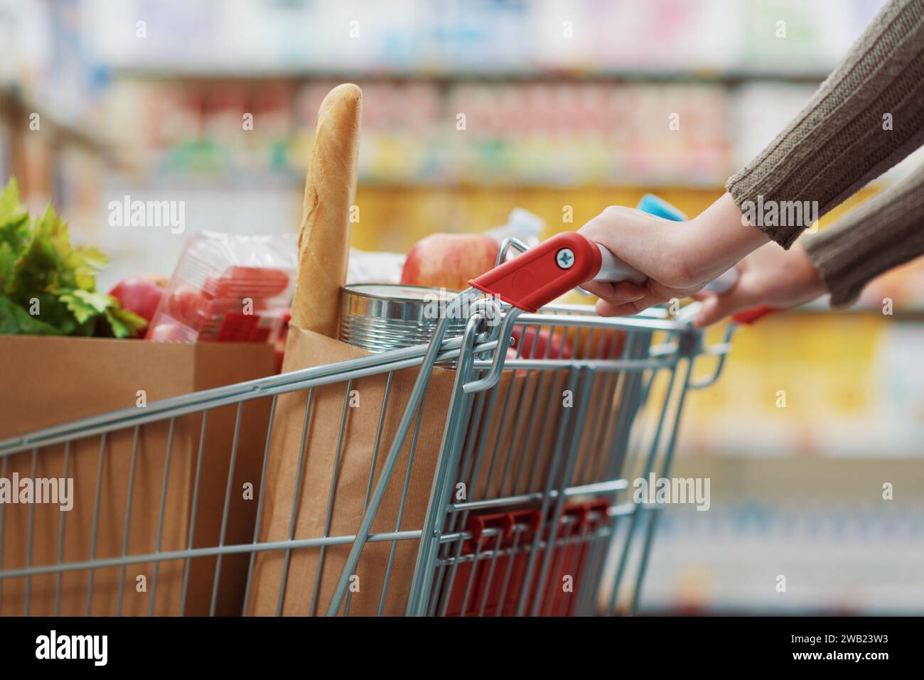 Weibliche Kundin, die Lebensmittel im Supermarkt kauft, schiebt einen vollen Einkaufswagen Stockfoto
