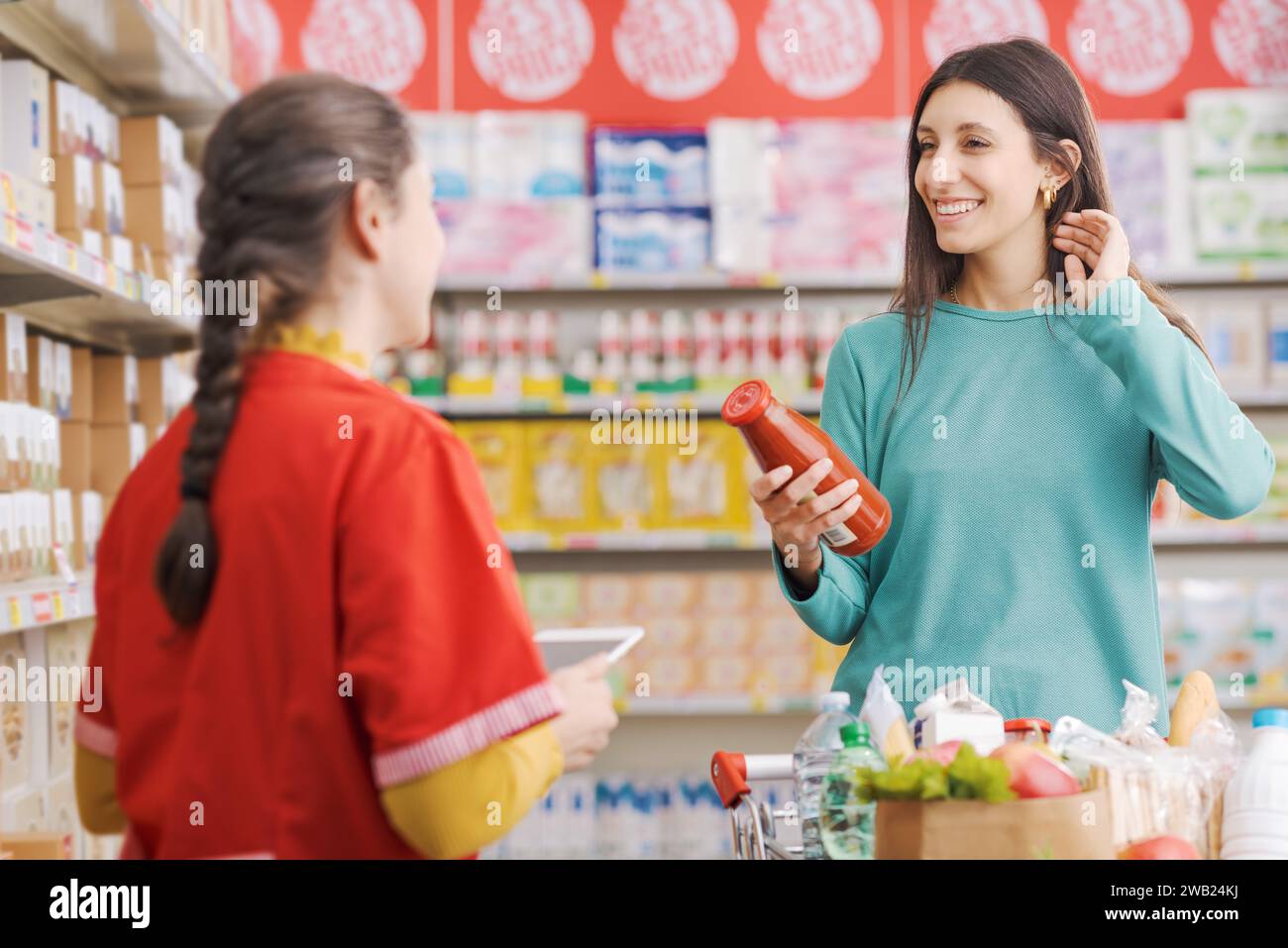 Freundlicher Mitarbeiter im Lebensmittelgeschäft hilft einer Frau, der Kunde lächelt und hält ein Produkt in der Hand Stockfoto