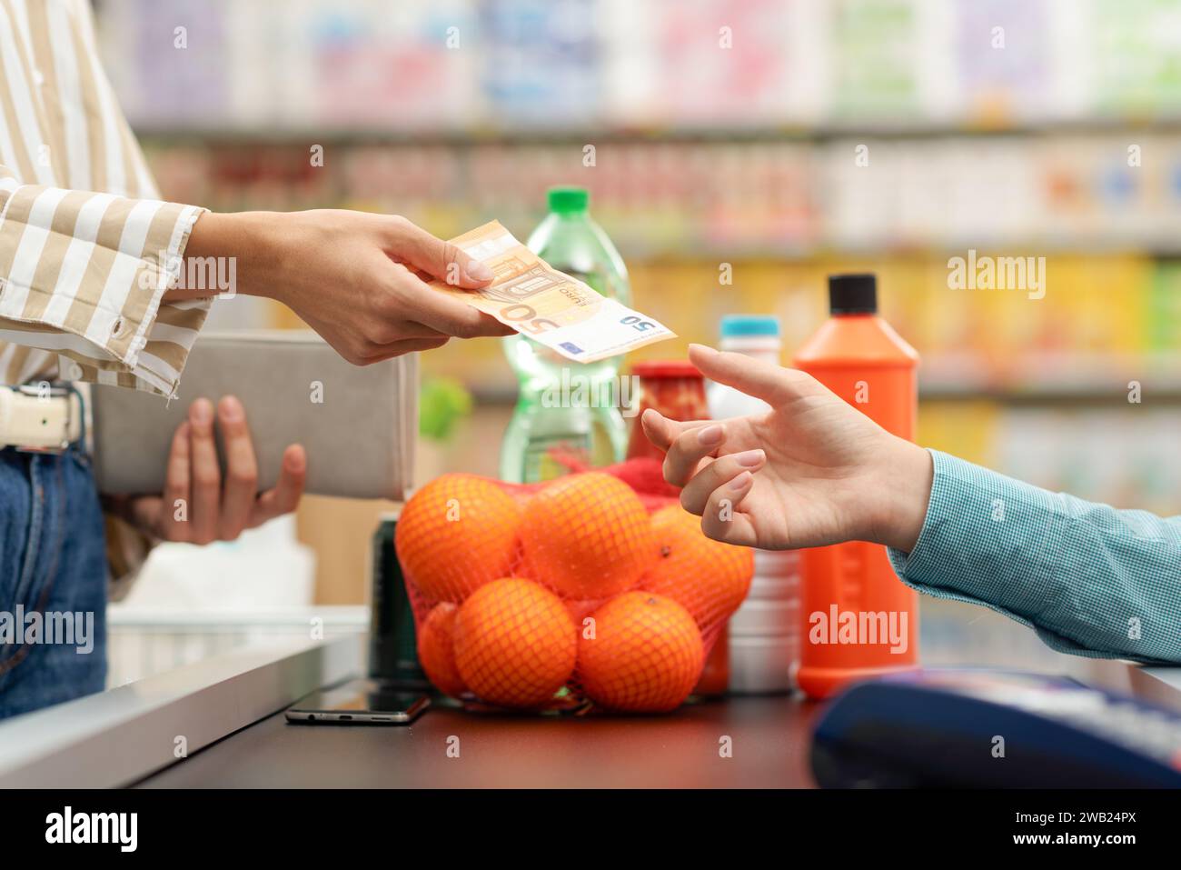 Die Frau, die an der Kasse des Supermarktes für ihre Lebensmittel bezahlt, gibt dem Kassierer Bargeld Stockfoto