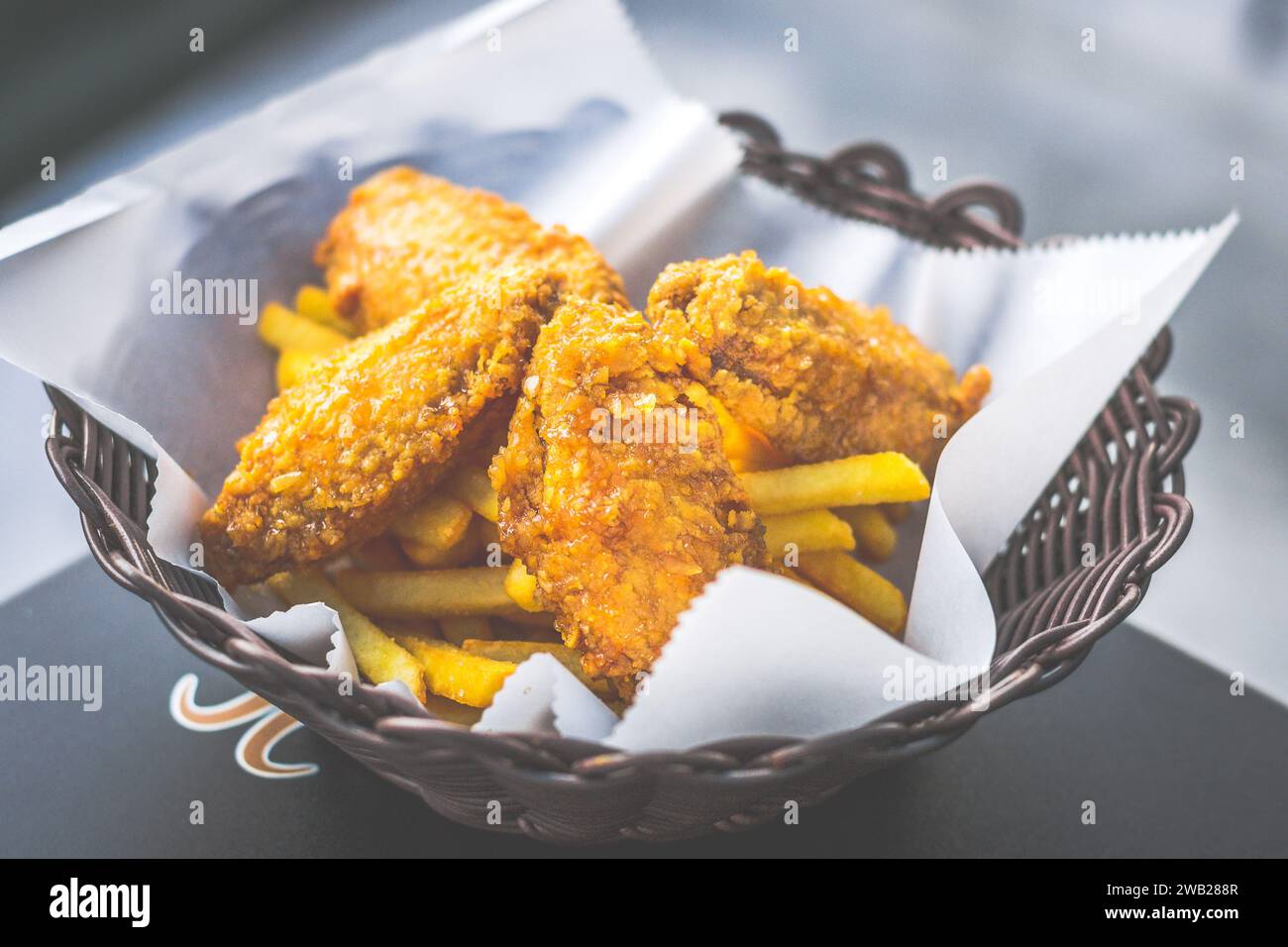Knusprige, goldbraune gebratene Hähnchenflügel, serviert in einem Korb mit Pommes frites Stockfoto