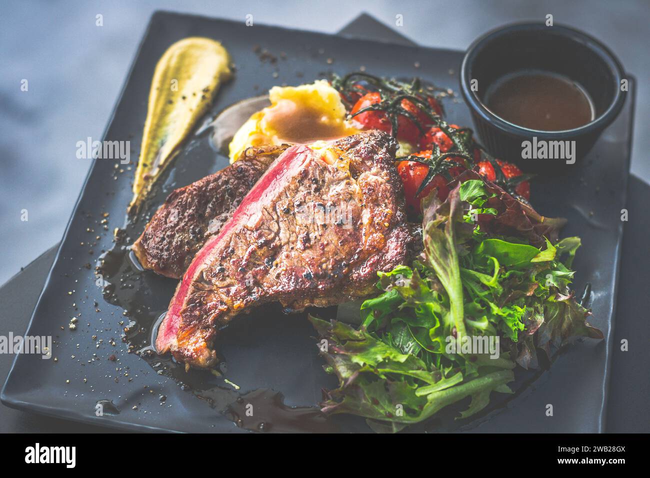 NZ Ribeye-Steak, gebraten bis mittelselten, begleitet von echter Country-cremigem Kartoffelpüree, Kirschtomaten auf Weinrebe, Garten-Mesclun-Salat Stockfoto