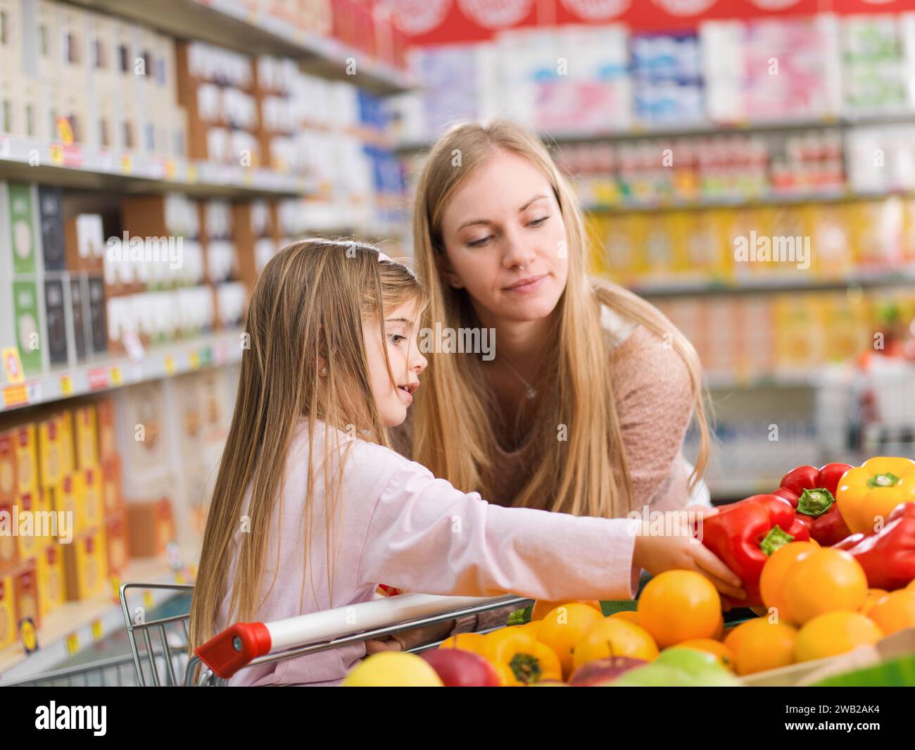 Mutter und Tochter kaufen zusammen Lebensmittel im Supermarkt, das Mädchen pflückt Gemüse in der Sparte Stockfoto