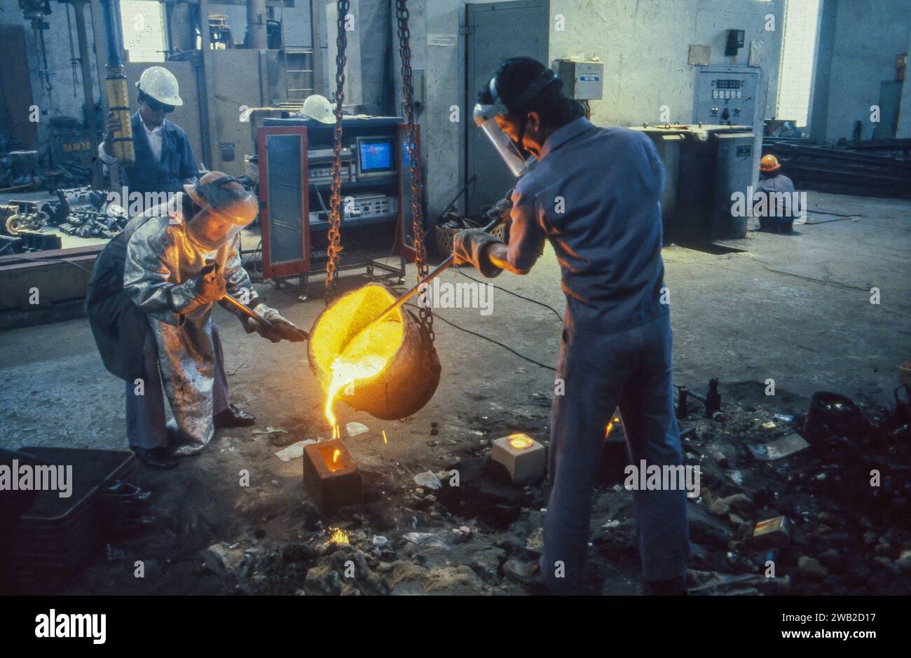 Indonesien, Bandung. Zwei Männer gießen geschmolzenes Metall in eine Form in einem Stahlwerk. Stockfoto