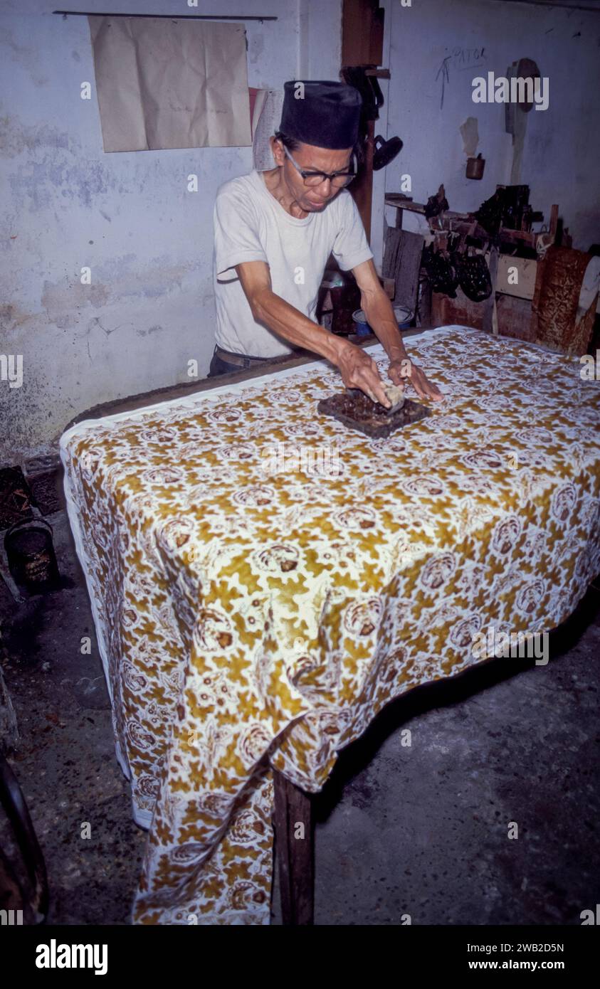 Indonesien, Java - in einer Batikfabrik trägt ein Mann Wachs auf ein Tuch mit einem Stempel auf und lässt es dann färben, um eine traditionelle Batikfabrik zu werden. Stockfoto