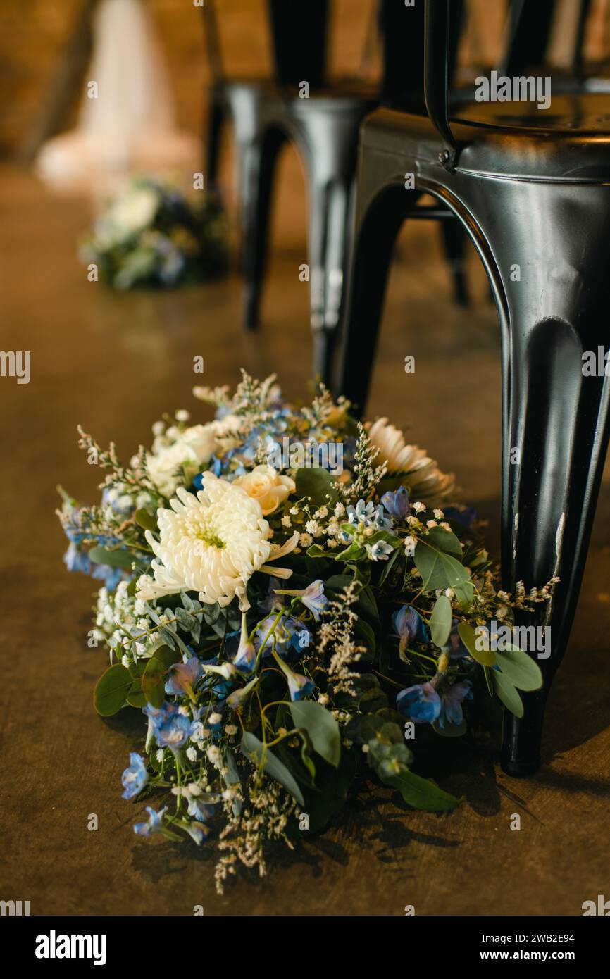 Blumenarrangements neben schwarzen Stühlen am Hochzeitsgang Stockfoto