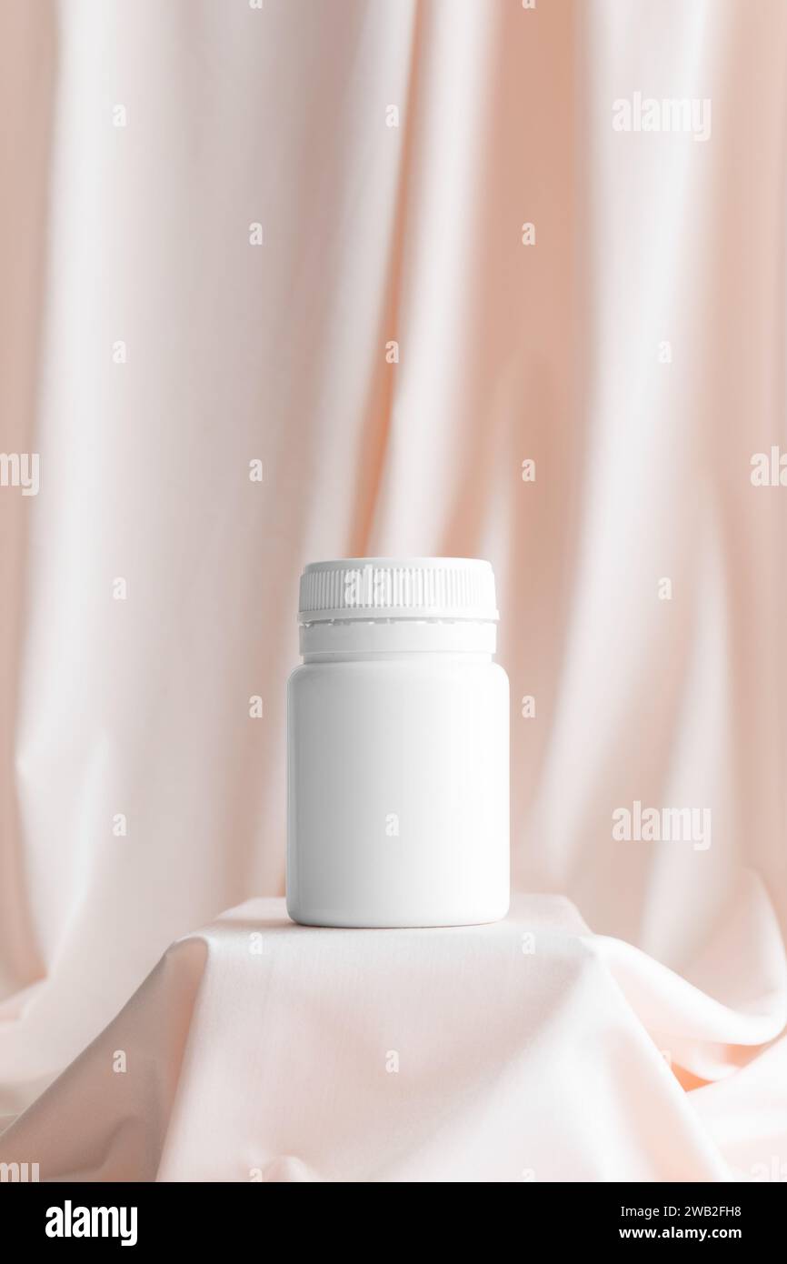 Weißes Pillenflaschenmockup auf dem weichen rosa Textil. Stockfoto