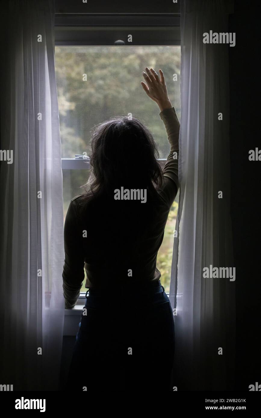 Eine ältere weiße Frau in Silhouette schaut aus dem Fenster Stockfoto