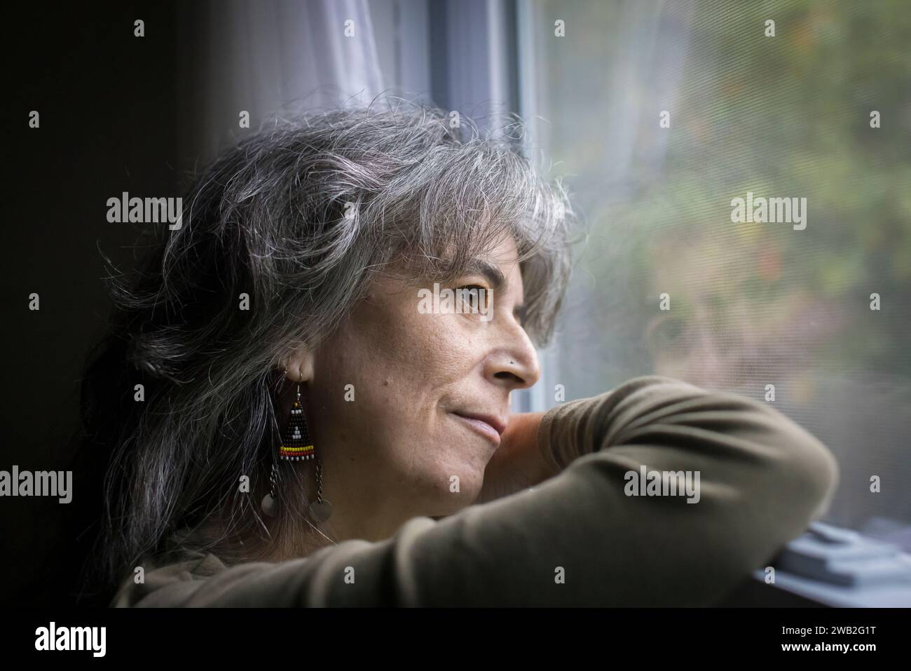 Eine ältere weiße Frau im Profil sieht deprimiert aus dem Fenster aus Stockfoto