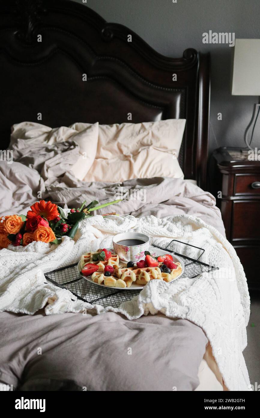 Waffeln und Kaffee auf einer Platte und Blumen zum Frühstück im Bett Stockfoto