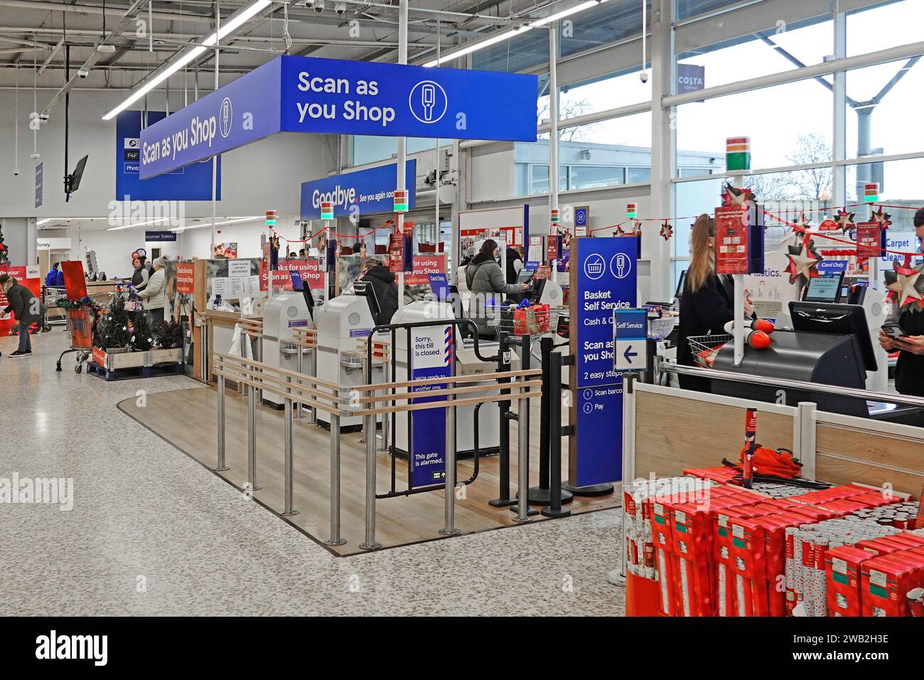 Scannen Sie beim Einkaufen von Schildern bei Käufern Kassen-Zahlungsbereich Kunden, die im Tesco Extra Supermarkt, einem Einzelhandelsunternehmen London England Großbritannien, einkaufen Stockfoto