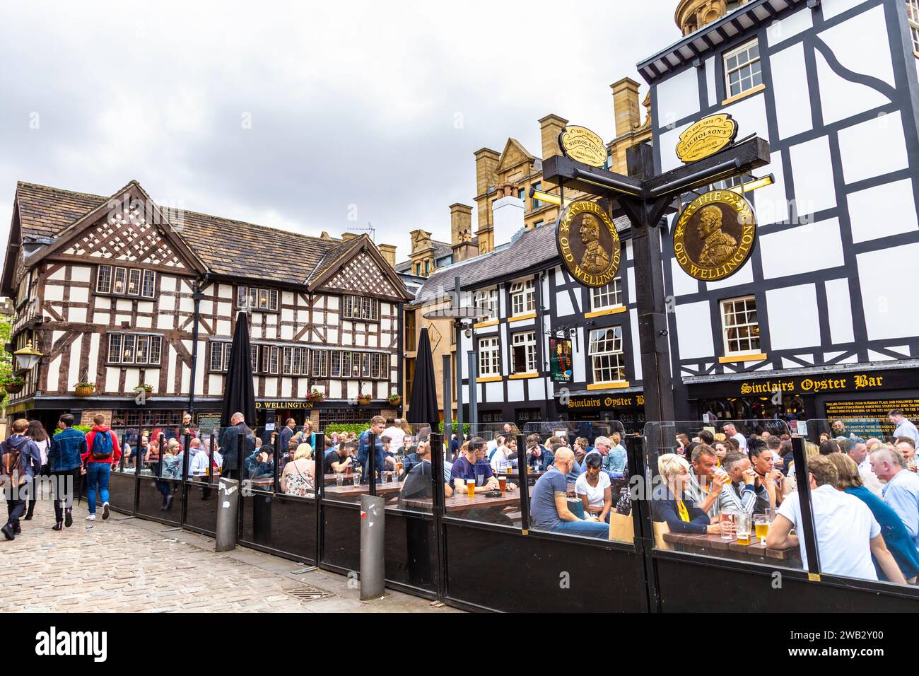 Menschen, die im Biergarten des denkmalgeschützten Old Wellington Pubs trinken, erbaut 1552 in Manchester, England Stockfoto