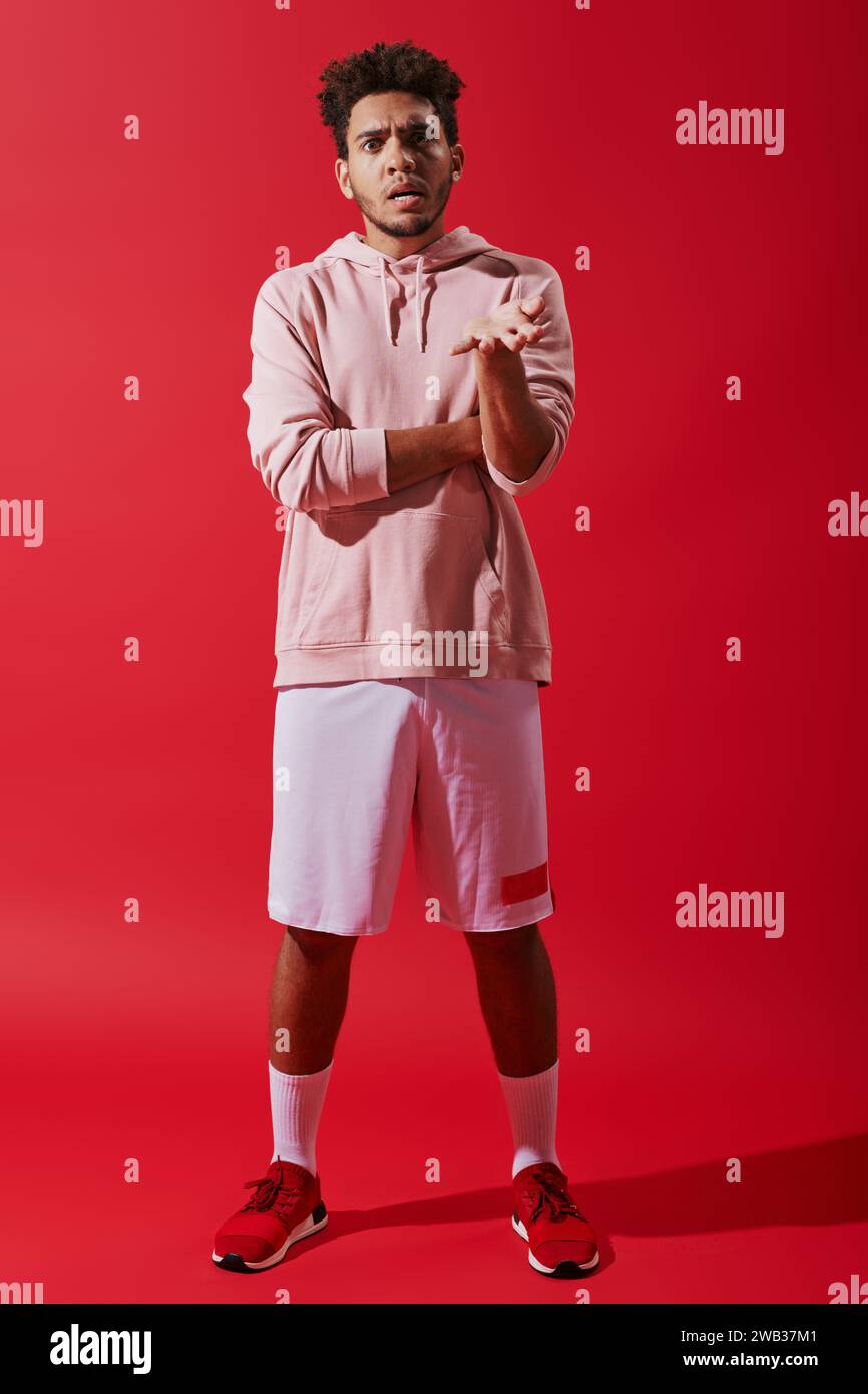 Ernsthafter after afroamerikanischer Sportler in Turnkleidung, der sich auf rotem Hintergrund beschwert Stockfoto