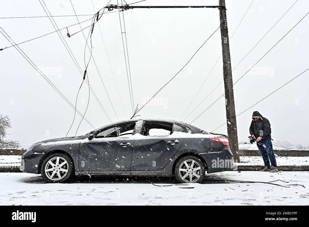 Zaporischzhia, Ukraine. Januar 2024. ZAPORIZHZHIA, UKRAINE - 8. JANUAR 2024 - Ein Mann filmt ein beschädigtes Auto unter den Übertragungsleitungen nach dem russischen Raketenangriff auf Zaporischzhia, Südostukraine. Quelle: Ukrinform/Alamy Live News Stockfoto