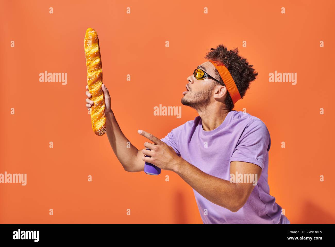 afroamerikanischer Mann in Sonnenbrille, der frisches Baguette und Limonade auf orangem Hintergrund ansieht Stockfoto