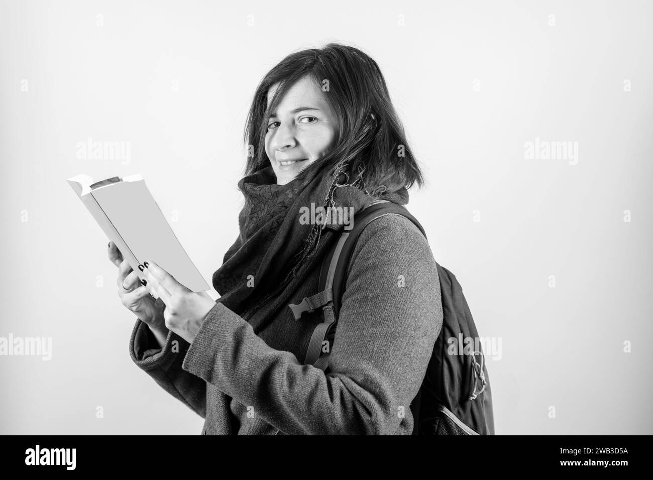 Attraktive junge Frau, die in die Kamera schaut, ein Buch liest, mit schwarz-weiß mit weißem Hintergrund. Lesekonzept. Stockfoto