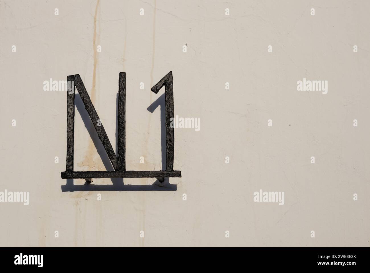 Beige Fassade eines Hauses in der Sonne. Metall N 1 an der Wand. Lanzarote, Kanarische Inseln, Spanien. Stockfoto