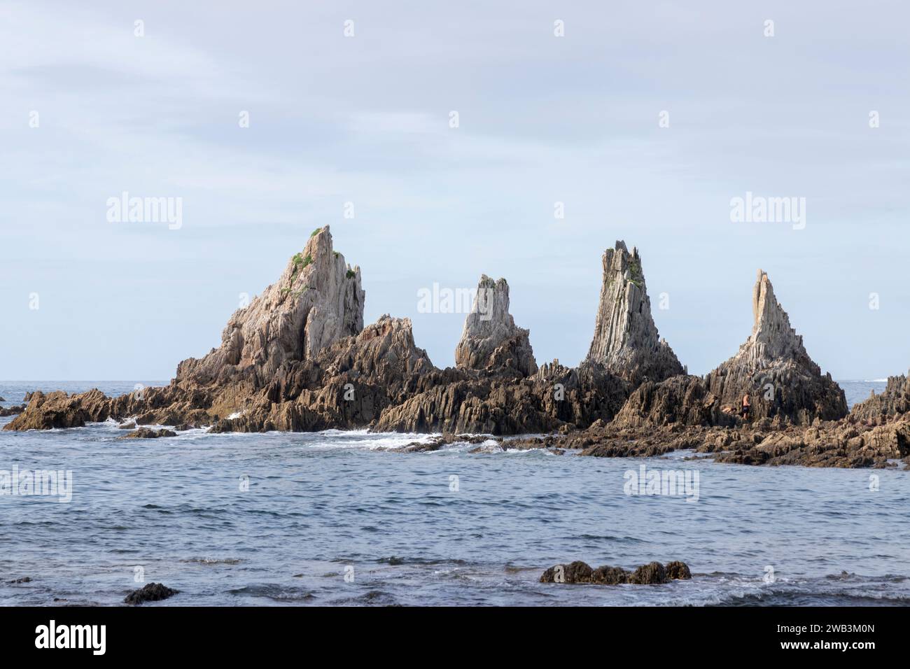 Felsformationen, die aus einem ruhigen Meer ragen, unter einem teilweise bewölkten Himmel, bilden eine ruhige, aber zerklüftete Küstenlandschaft in asturien Stockfoto