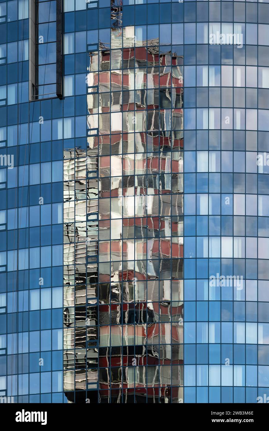 Das Foto zeigt eine Nahaufnahme der Fassade eines Glashochhauses. Die glatte, reflektierende Oberfläche des Gebäudes erfasst ein verzerrtes Bild eines Stockfoto