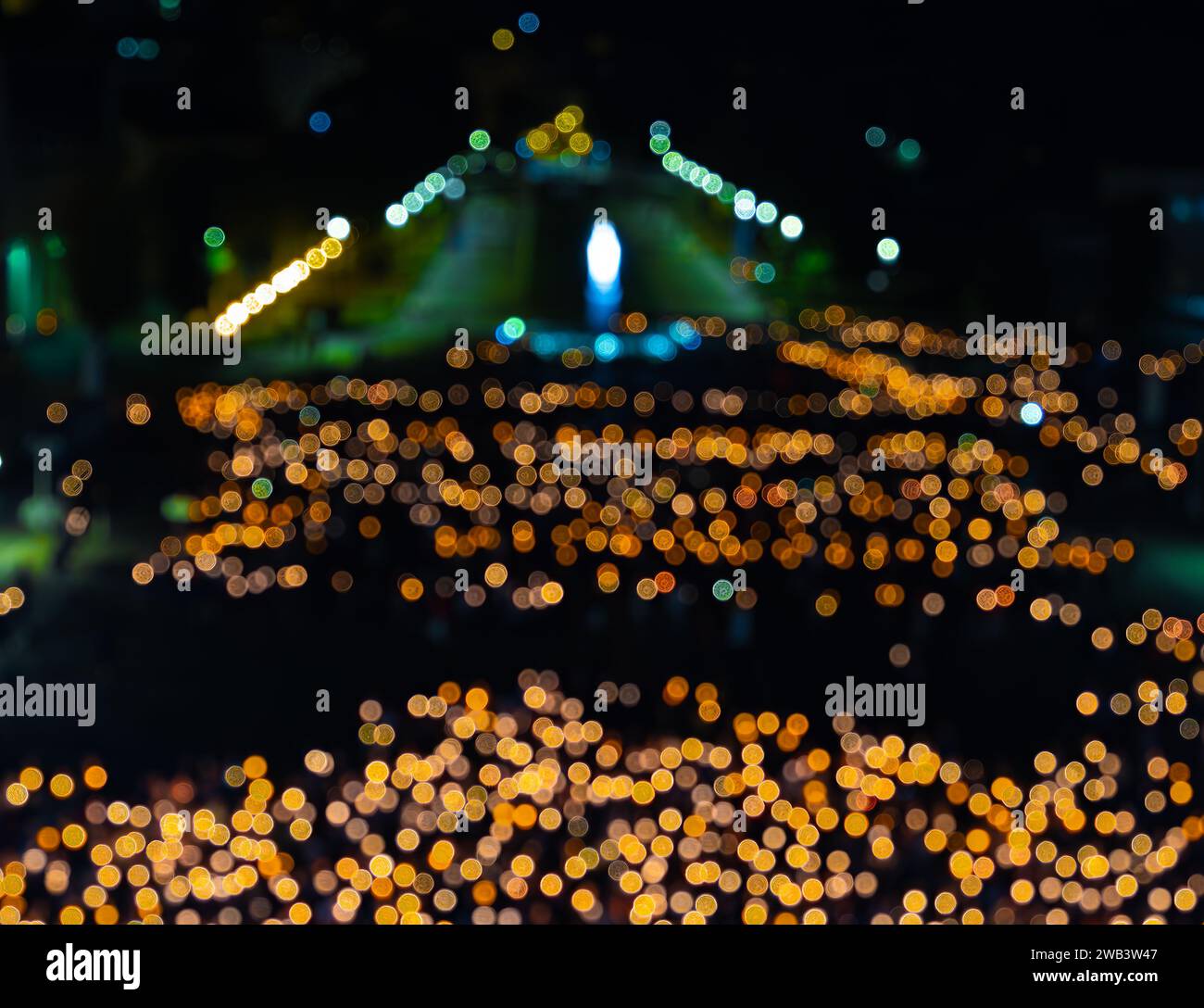 Absichtlich verschwimmerte Pilgermenge mit brennenden Kerzen, die bei einer nächtlichen Pilgerprozession in Lourdes beteten. Stockfoto