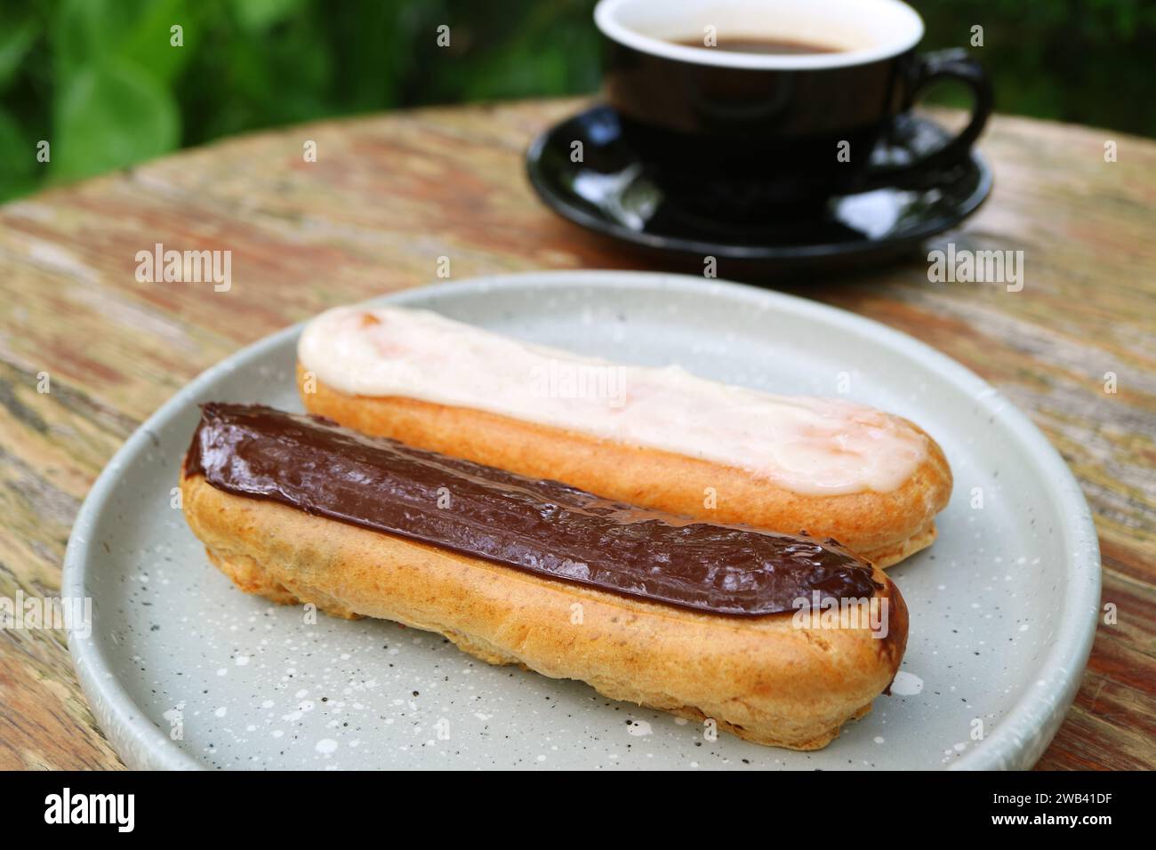 Teller Schokolade und Vanilleeclairs mit einer Tasse heißem Kaffee im Hintergrund Stockfoto