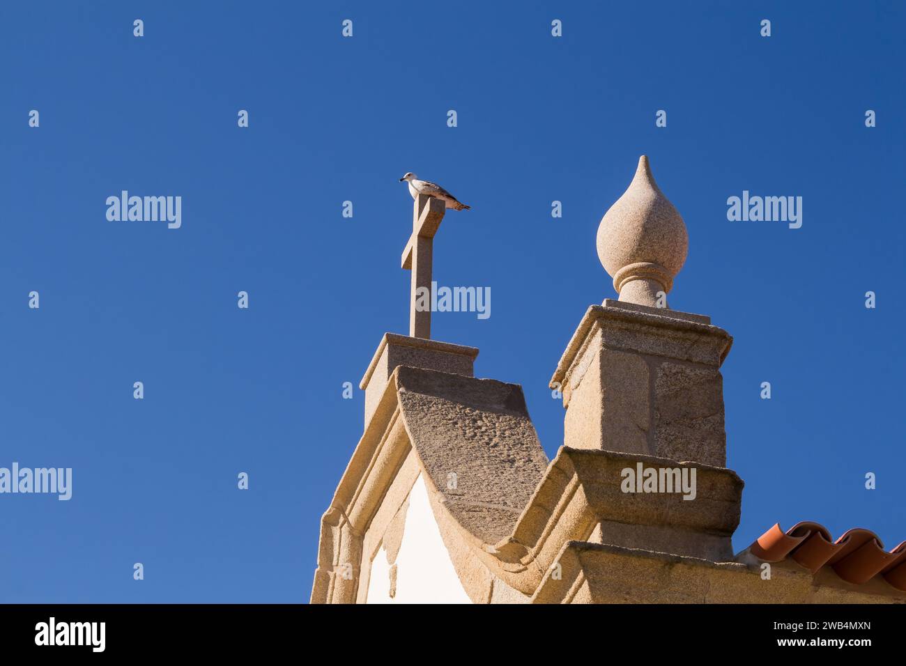 Kleine weiße Kapelle im traditionellen portugiesischen Stil an der Küste des Atlantiks, Kreuz auf dem Dach mit einer Möwe darauf. Leuchtend blau s Stockfoto