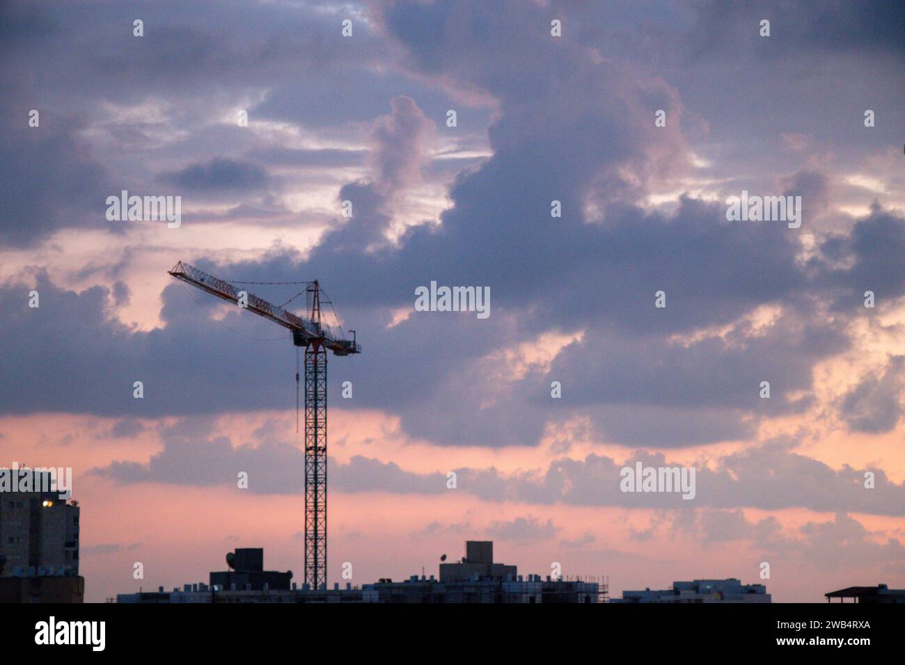 Ein Kranturm über dem Wohnbauprojekt. Bau von Eigentumswohnungen. Sonnenuntergang, goldene Stunde, mit Wolken Stockfoto