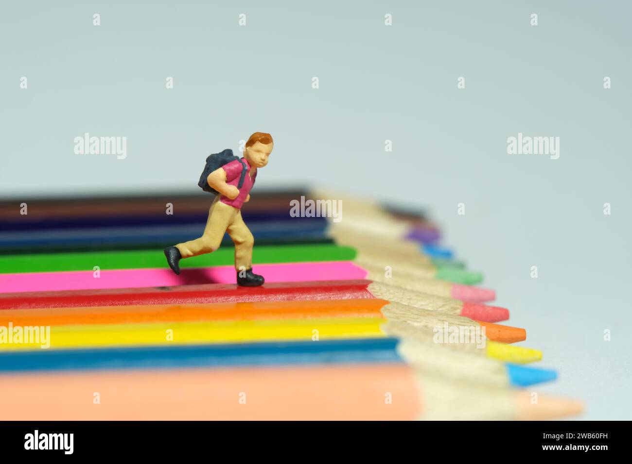 Miniatur Tiny People Spielzeug Fotografie. Ein Junge mit Schulrucksack, der über dem Buntstift läuft. Isoliert auf grauem Hintergrund. Bild Foto Stockfoto