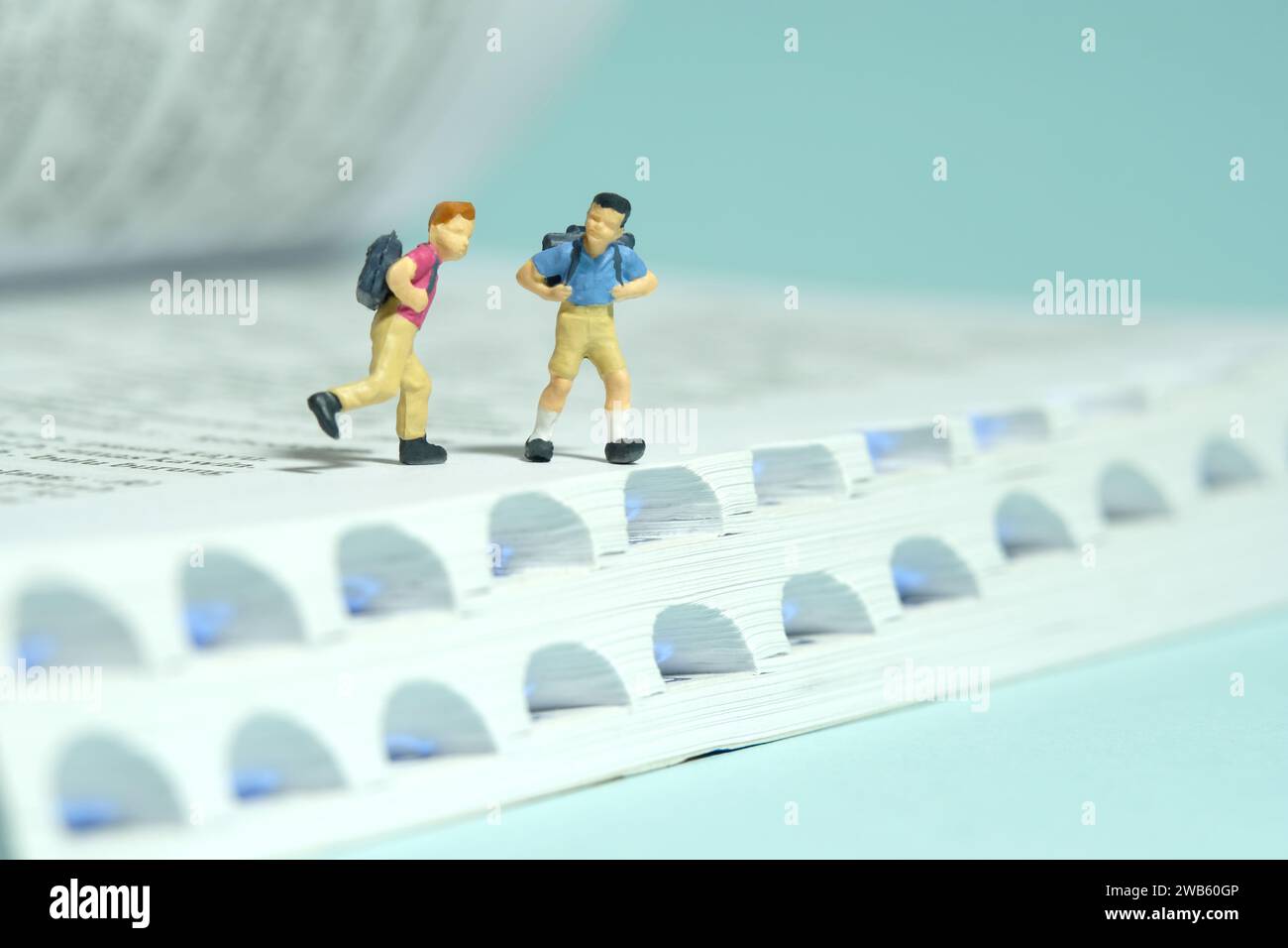 Miniatur Tiny People Spielzeug Fotografie. Zwei Jungen mit Schulrucksack, die über dem Buch laufen. Isoliert auf blauem Hintergrund. Bild Foto Stockfoto