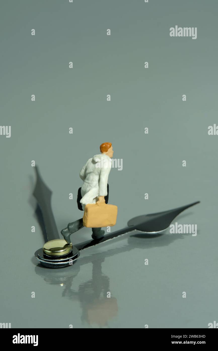 Miniatur-Kleinkinder-Spielfiguren-Fotografie. Ein Geschäftsmann, der über dem schwarzen Uhrzeigersinn läuft und eine Aktentasche trägt. Isoliert auf grauem Hintergrund. Bild Foto Stockfoto